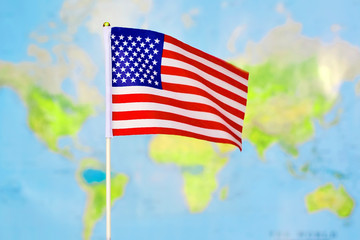  The small flag of the United States waving in the wind against the background of the world map.Сoncept of  USA Independence Day . Celebrated on July 4.