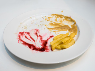 Empty dish after food, red and yellow sauce food leftovers and french fries on a white plate.