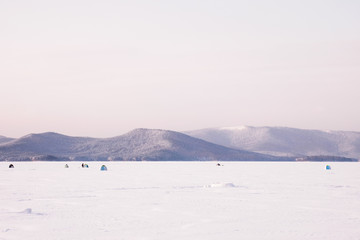 Landscape with fishermen and tilts tents on winter lake covered with snow and ice. Winter extreme sports - ice fishing.