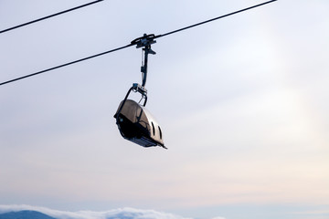 Closeup ski lift on the cable car with a closed cabin on the background of snow-capped mountain peaks, sun. Concept place for inscription, sunrise, sunshine, sunset