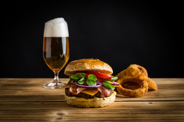 Cheeseburger mit Bier und Zwiebelringe auf Holz