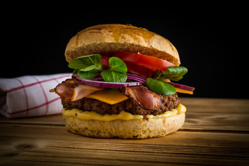 Regionaler und selbstgemachter Burger mit Geschirrtuch auf Holzbrett und schwarzen Hintergrund
