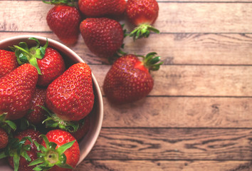 Flat lay of fresh strawberry in a pink bowl on wooden board. Healthy food concept.