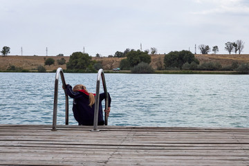 editorial,young girl in a tracksuit is standing on a wooden pier and looks into the lake