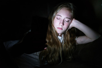 Depressed girl lying down on a couch in the dark while using her smartphone. The light from the screen is illuminating her face.