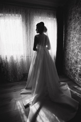 Beautiful young bride stand in front of the window in her room. Black and white