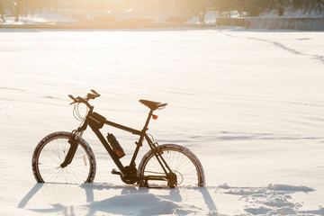 Fototapeta na wymiar Winter season cycling. Black bicycle on the snow inte city center. Sport at any time of year concept.