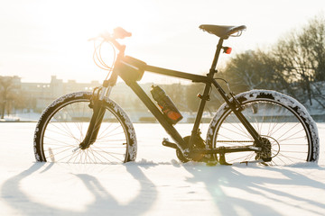 Winter season cycling. Black bicycle on the snow inte city center. Sport at any time of year concept.