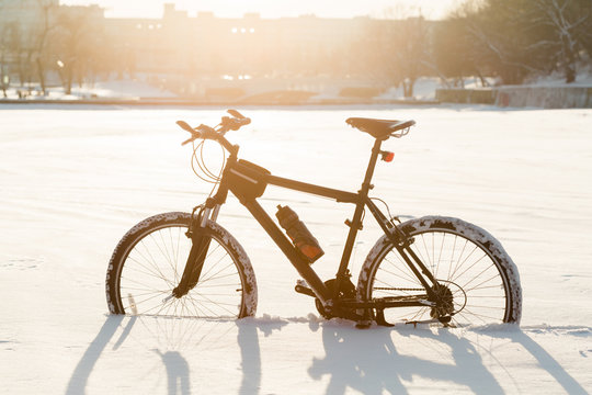Winter season cycling. Black bicycle on the snow inte city center. Sport at any time of year concept.