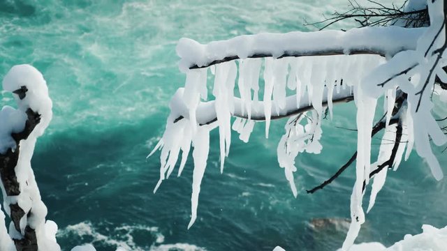 An icy twig of a tree with icicles against the blue water of Niagara Falls. Winter season
