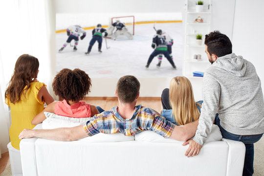 sport, people and entertainment concept - happy friends watching ice hockey game on projector screen at home