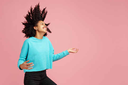 Portrait of excited african american young woman with bright smile dressed in casual clothes dance with invisible guitar over pink background.