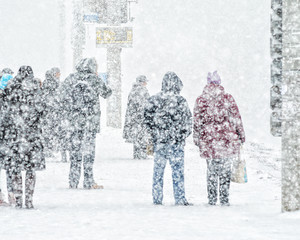 Blizzard in an urban environment. People on bus stop in snowfall. Abstract blurry winter weather background