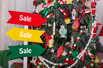 Multicolored sign with informative inscription of sale near christmas tree. Sales on Christmas and New Year holidays. Black Friday, Christmas discounts, New Year discounts.
