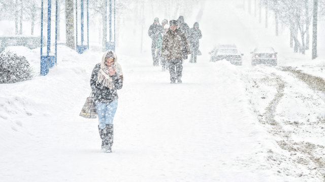 Young girl walk through snowfall resisting the pressure of a snowfall. Blizzard in an urban environment. Abstract blurry winter weather background