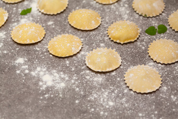 Tasty raw ravioli with flour on dark background. Process of making italian ravioli.