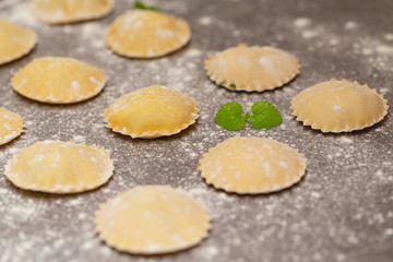 Fototapeta na wymiar Tasty raw ravioli with flour on dark background. Process of making italian ravioli.