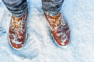 First person view of legs in brown boots in the snow. Snow on boots while walking in winter