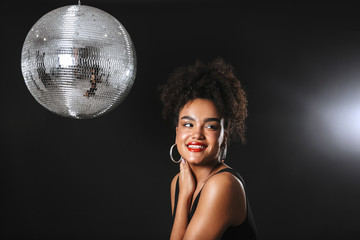 Image of beautiful african woman standing with silver disco ball, isolated over black background