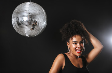 Image of adorable african woman standing with silver disco ball, isolated over black background