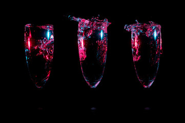 Small splashes of clear liquid glowing in red with blue highlights in three glasses in a row on a black background