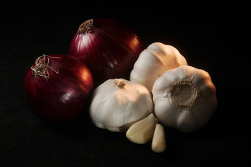 Composition of two red onions next to three heads of garlic on a black background