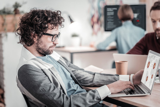 Concentrated curly-haired man working at his laptop