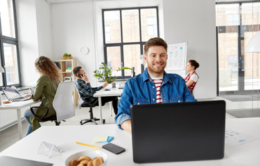 business, technology and people concept - happy smiling creative man with laptop computer working on user interface design at office