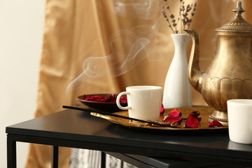 Golden teapot with cups and aroma stick on dark table