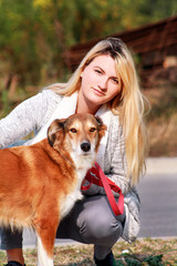 Pretty girl with his Shetland sheepdog dog at nature park outdoor is standing and posing in front of camera. Portrait of owner and Rough collie dog enjoys, resting and petting together on city street.
