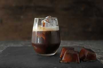 Glass of cold coffee with ice cubes on slate plate