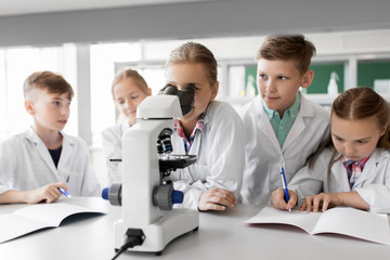 Fototapeta premium education, science and children concept - kids or students with microscope studying biology at school laboratory