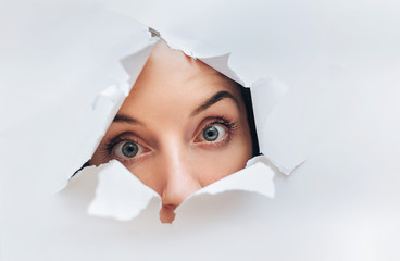 Surprised woman face. Cute attractive woman looking through hole. Copy space for advertising, to...