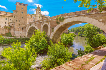 Fototapeta premium View of the Tiber island or Isola Tiberina with Ponte Fabricio and church Chiesa di San Giovanni Calibita in sunny day, Rome, Italy