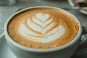 Close up of cup of cappuccino with beautiful latte art on a grey wooden table in a cafe.