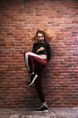 Full length photo of attractive hip hop dancer or sporty girl, dancing against brick wall