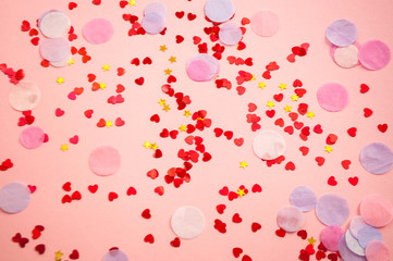 Blurred beautiful heart and stars shaped red confetti on pink background.