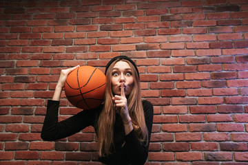 Portrait of european woman 20s, standing against brick wall and holding basketball