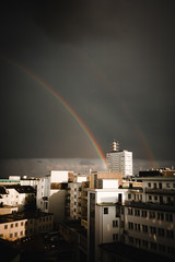 Regenbogen über einer Stadt. Doppelregenbogen, graue Wolken, dunkle Stimmung.