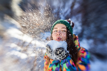 Beauty Winter Girl Blowing Snow in frosty winter Park. Outdoors. Flying Snowflakes. Sunny day. Backlit. Joyful Beauty young woman Having Fun in Winter Park.