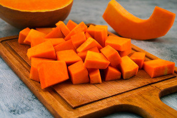 Pieces of orange pumpkin on the cutting Board. Raw vegetables. Vegetarian food. Light background.