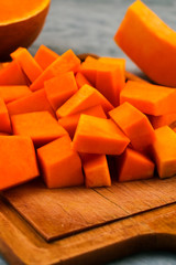 Preparation of raw pumpkin. Pieces of orange pulp on a wooden Board. Vegetarian food. Raw vegetables. Light background.