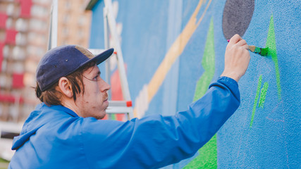 Guy draws paint on the wall on the street