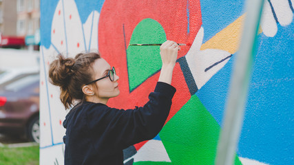 Girl paints mural on the wall with a brush, color wall - obrazy, fototapety, plakaty