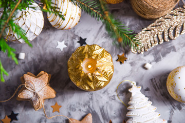 Christmas decorations on a gray background with golden candles among the shiny stars and green Christmas tree branches. Top view