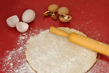 Flour, dough, wooden rolling pin, eggs and walnuts on a red background.