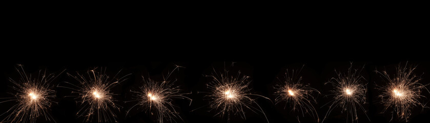 A burning sparkler on a black background with copy space for you design, panorama, new year concept.