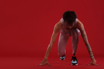 A strong athletic, woman sprinter, reay to running on red background wearing in the sportswear,...