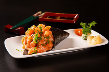 Salmon temaki sushi on white plate in black background.