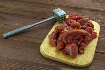 Meat beef cut into pieces lies on a wooden Board. Metal Hammer for beating meat